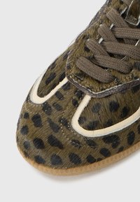 Tenisice s uzorkom leoparda, gornji dio od teksturirane zelene i smeđe krzna, kontrastni bijeli detalji i smešasti pertle. Gumeni đon s blago prozirnom ivicom.