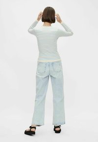 Světle modrý a bílý pruhovaný top s dlouhými rukávy, kombinovaný se světle modrými riflemi s vysokým pasem a černými sandály, z pohledu zezadu.