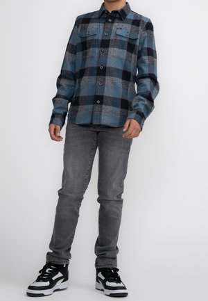Flannel shirt in blue, black, and gray plaid with two chest pockets; paired with gray slim-fit jeans and black-and-white sneakers.