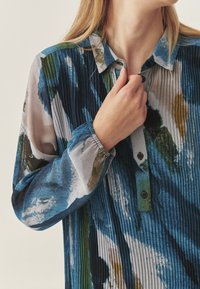 Mehrfarbiges Hemd mit Knopfleiste und strukturiertem, plissiertem Design. Es enthält Blau-, Grün- und Gelbtöne und hat lange, elastische Ärmel.