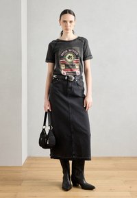 T-shirt grafica nera con stampa colorata, abbinata a una gonna maxi in denim nera. Gli accessori includono una borsa nera e stivali neri alla caviglia.