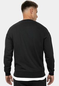 Felpa nera con texture a coste, collo girocollo e spalle cadenti; presenta uno strato bianco che sbuca dall'orlo in vita.