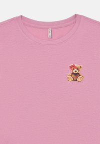 Rosa Baumwoll-T-Shirt mit rundem Halsausschnitt, das einen kleinen, gestickten braunen Teddybär mit einer roten Schleife am linken Ohr zeigt.