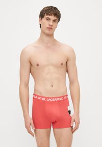 Boxers pour hommes rouges avec une coupe ajustée, dotés d'une ceinture avec logo et d'une touche de dessin animé sur le côté. Fabriqués en tissu doux et extensible.