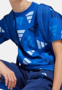 Maglietta blu con motivi geometrici in diverse tonalità di blu e bianco. Il tessuto è morbido e presenta un collo rotondo e maniche corte.