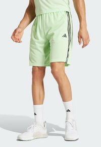 Pantaloni sportivi verde chiaro con strisce nere laterali, abbinati a scarpe da ginnastica bianche e calze con accenti neri.