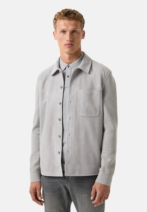 Grau Wildlederjacke mit klappbarem Kragen, Fronttasche und Knopfverschluss, kombiniert mit einem hellgrauen Hemd darunter. Weiche Textur.