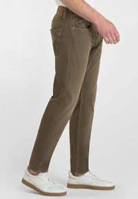 Pantalon vert olive en tissu doux et texturé, avec une coupe droite, cinq poches et une patch en cuir marron au niveau de la taille.