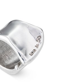 Anillo de plata con superficie lisa y pulida, con una forma geométrica única y un logo grabado en la banda interior.