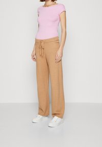 Pink fitted top and light brown drawstring pants with a soft texture. Model wearing white sneakers. Simple, loose design overall.