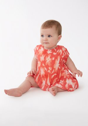 Vestido de bebé con estampado floral de coral, de manga corta, diseño plisado, tejido suave y patrones decorativos de flores. Bebé sentado con los pies descalzos.