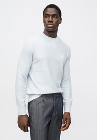 Gaiši zils ribots džemperis ar apaļu apkakli un nelielu logotipa plāksteri. Kombinēts ar tumšām svītrainām biksēm, rādot fakturētas auduma detaļas.