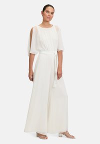 Fehér overál rövid, légies ujjal, ráncolt mellel és derékpánttal. Széles lábú nadrágokkal rendelkezik, és könnyed, áttetsző textúrája van.