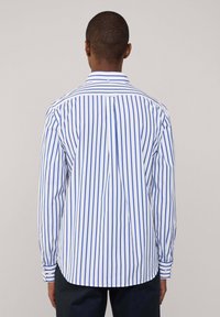 Camisa de botonadura a rayas en blanco y azul, con mangas largas, cuello extendido y detalle de pliegues en la parte posterior. Los puños ajustables cuentan con botones.