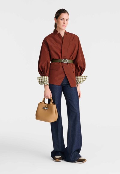 Brown oversized shirt with green check cuffs, belted with a green belt, paired with dark denim flared pants and a tan handbag.