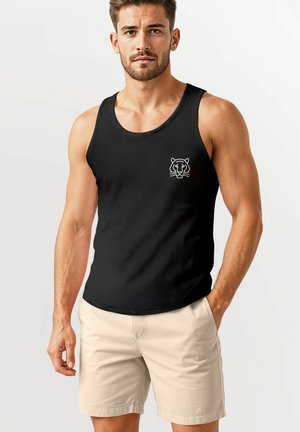 Black tank top made of cotton blend, featuring a white tiger graphic on the left chest. Worn with beige shorts, showcasing an athletic fit.