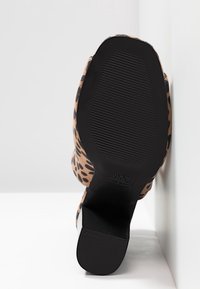 Chaussure à talon haut imprimé léopard montrée par la semelle avec semelle extérieure en caoutchouc noir texturé et talon bloc sur fond blanc.