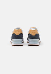 Paire de baskets New Balance vues de dos, en daim bleu marine, avec des accents beiges et des semelles intermédiaires blanches sur fond blanc.