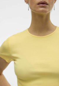 T-shirt gialla a coste con maniche corte e scollo rotondo. Texture liscia, design aderente e dettagli delle cuciture delicati.