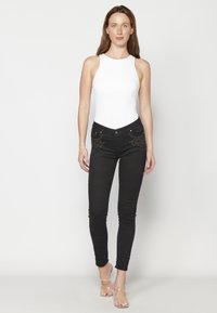 Black skinny jeans with embellished front pockets paired with a white sleeveless bodysuit. Clear slip-on heels complete the look.