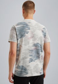 T-shirt à manches courtes en beige clair avec des motifs rayés abstraits bleus et roses. Tissu doux et coupe classique.