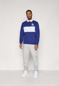 Mørkeblå langærmet polo med hvid vandret stribe, LA logo, parret med grå cargo sweatpants. Model iført hvide sneakers.