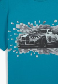 Lys turkise t-shirt med en stiliseret grå racerbilsdesign og pixeliserede eksplosions-effekter i baggrunden, der understreger hastighed og bevægelse.