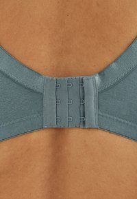 Rückansicht einer Person, die einen türkisfarbenen BH trägt, der mit zwei Reihen Haken auf glatter Haut befestigt ist.