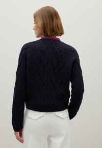 Dunkelblaues Strickpullover mit einem Kabelstrickdesign, gerippten Bündchen und Saum sowie einem Rundhalsausschnitt. Getragen mit weißen Jeans, zeigt die Rückansicht.