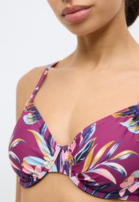 Μπικίνι τοπ σε μωβ χρώμα με floral σχέδιο, συγκεντρωμένη ύφανση, ρυθμιζόμενους ιμάντες και έναν κόμπο στο κέντρο με μοτίβα φύλλων σε μπλε και ροζ.