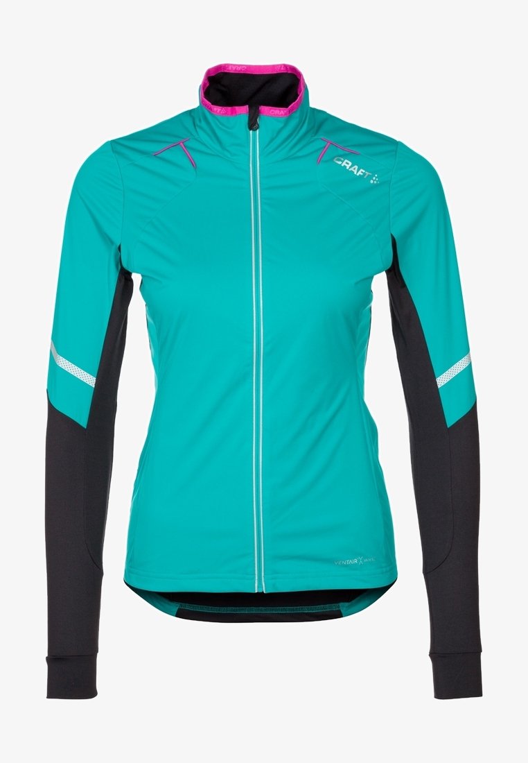 Chaqueta deportiva para mujer de manga larga en verde azulado y negro con franjas reflectantes, ribete rosa en el cuello, cremallera frontal y logo de Craft en el pecho.