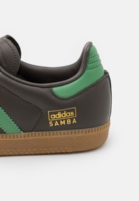 Schwarze Ledersneaker mit grünen Akzenten und goldfarbigem "adidas SAMBA"-Logo. Verfügt über eine strukturierte Gummisohle und einen gepolsterten Schaft für zusätzlichen Halt.