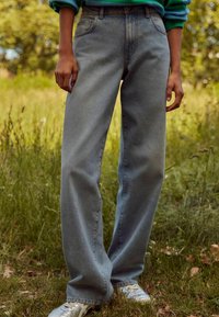 Jeans din denim de culoare albastră deschisă, cu talie înaltă și picioare largi, având un finisaj ușor decolorat. Dispun de un design clasic cu cinci buzunare și de detalii subtile de whiskering.