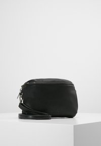 Musta nahkainen laukku, jossa on pyöreä muoto, vetoketjukiinnitys ja irrotettava olkahihna. Ominaisuuksiin kuuluu sileä pinta ja minimalistiinen muotoilu.