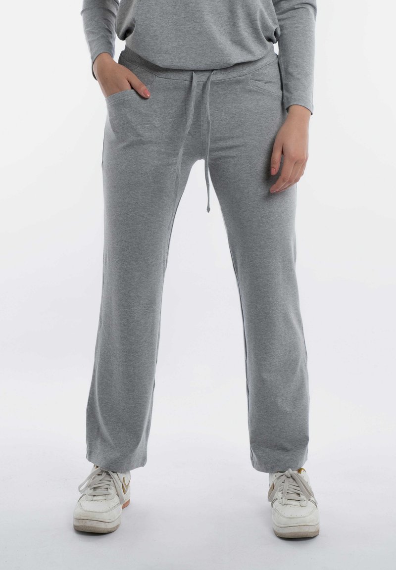 Grijze sweatshirtbroek met een trekkoord in de taille en zijzakken. Zachte textuur met een ontspannen pasvorm, taps toelopend bij de enkels. Witte sneakers.