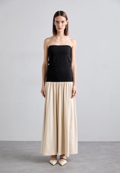 Haut noir sans bretelles avec une texture lisse associé à une jupe longue, froncée de couleur crème. Le modèle porte des talons beiges pointus avec des brides noires.