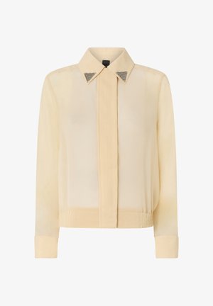 Camicia a maniche lunghe color crema con colletto appuntito arricchito da punte decorative in metallo triangolari argentate, patta frontale nascosta e fascia in vita aderente.