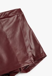 Burgunderfärgade shorts i konstläder med en slät textur, hög midja och rena linjer, som framhäver en skräddarsydd och stilren design.