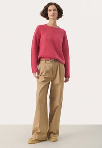 Roze geribbelde trui met lange mouwen, gecombineerd met hooggesneden, beige wijde broek en beige schoenen. Eenvoudig, textuurrijk ontwerp.