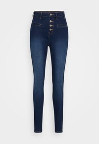 Jeans skinny de talle alto en azul oscuro, con cuatro botones frontales y dos bolsillos de ojal, exhibidos sobre un fondo blanco.