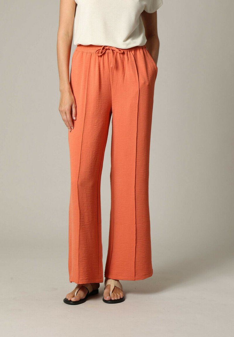 Lichte, gestructureerde oranje broek met een tailleband met trekkoord, zijzakken en wijde pijpen, gecombineerd met een eenvoudig wit shirt en sandalen.