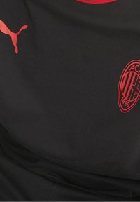Camisa deportiva de tela negra con acentos rojos. Muestra un logo rojo de Puma a la izquierda y un emblema del AC Milan a la derecha.