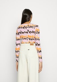 Top cropped de mangas longas com um padrão ondulado em rosa, laranja e castanho, combinado com calças brancas de cintura alta.