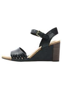 Sandale à talon noir en wedge avec une tige en cuir texturé, un design à franges, une lanière de cheville réglable et une semelle en liège avec un talon en bois.