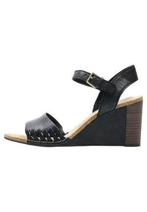 Sandale à talon noir en wedge avec une tige en cuir texturé, un design à franges, une lanière de cheville réglable et une semelle en liège avec un talon en bois.