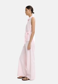 Różowa bezrękawnik z guzikami, związaną w talii, połączony z szerokimi różowymi spodniami. Gładki materiał z subtelnym wzorem.