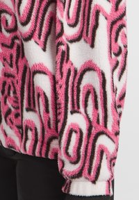 Fleece pullover featuring a pink, black, and white abstract pattern; soft texture; long sleeves with ribbed cuffs; relaxed fit.