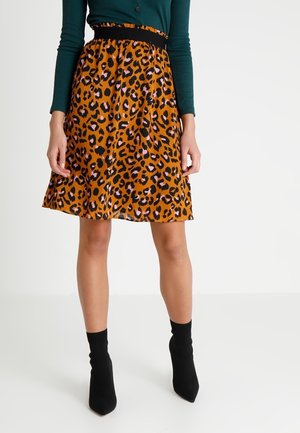 Jupe imprimé léopard en orange et noir, avec une coupe évasée et une texture lisse, associée à des bottines à talons noires.