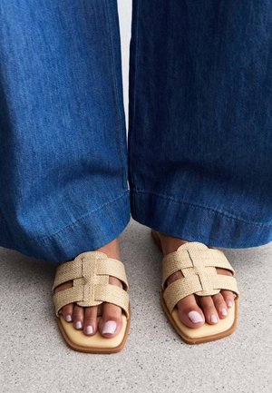 Beige neulottuja liukuva kenkiä, joissa on neliömaiset varpaat ja ristikkäiset hihnat. Yhdistetty leveälahkeisiin sinisiin farkkuihin, joissa on sileä pinta.