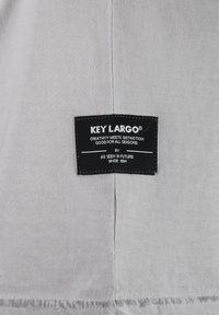 Etiqueta negra sobre tela gris; el texto de la etiqueta dice "KEY LARGO", con un eslogan y detalles de la marca. La tela es suave con un ligero brillo.